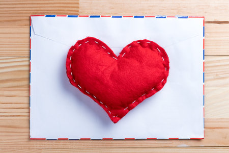 Red homemade heart on a love letter on Valentine's Day. Blank envelope. Natural wooden table.