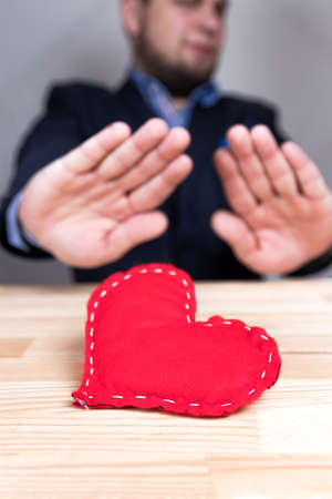 Elegant man in a suit rejecting homemade red heart on Valentine's Day. Natural wooden table.の写真素材