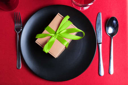 Romantic dinner table setting on Valentine's Day. Gift or present on a plate. Pantone greenery color theme. Date in restaurant.の写真素材
