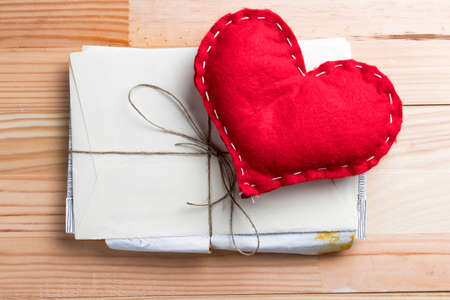 Red homemade heart on a bunch of love letters on Valentine's Day. Natural wooden table.の写真素材