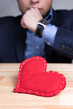 Elegant man in a suit with homemade red heart on Valentine's Day. Natural wooden table.の写真素材