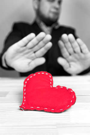 Elegant man in a suit rejecting homemade red heart on Valentine's Day. Natural wooden table. Black and white.の写真素材