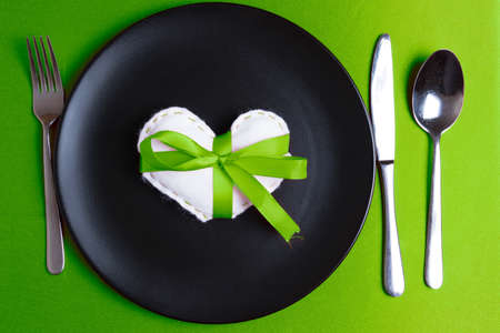 White heart on a plate on Valentine's Day. Elegant cutlery. Pantone greenery color theme. Green ribbon bow.の写真素材