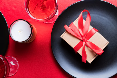 Romantic dinner table setting on Valentine's Day. Gift or present on a plate. Date in restaurant. Wine and candle.の写真素材