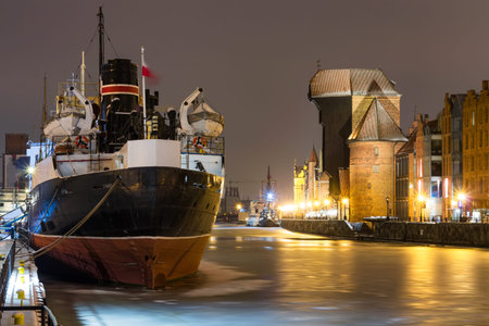 Historic tenement houses in the city of Gdansk, Poland during winter at night. Old ship and crane.