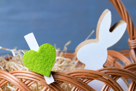 Greenery heart with spring easter bunny in wicker basket. Natural wooden background.