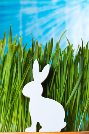 Easter bunny wooden figurine sitting in the grass. Spring time concept. Warm sun flare.の写真素材
