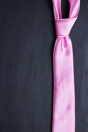 Pink elegant tie on black textured background. Doing business fashion abstract concept. Copy space on the left.の写真素材