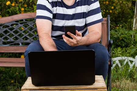 Young business man or entrepreneur with laptop and smartphone working from the garden. Freelance outside of office freedom.の写真素材