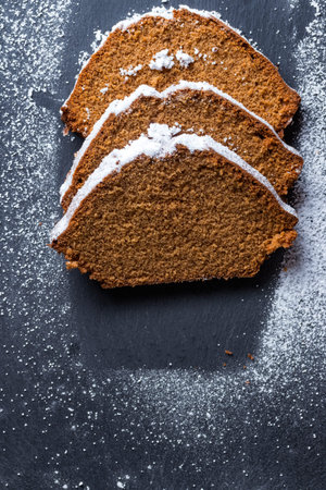 Homemade baked sweet gingerbread slices covered with powdered sugar on a black kitchen slate plate.の写真素材