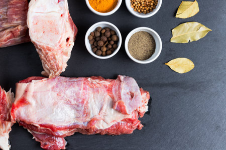 Fresh colorful spices in white bowls and chunks of raw beef meat on black kitchen slate plate background. Copy space in the bottom right corner. Flat lay top view.の写真素材