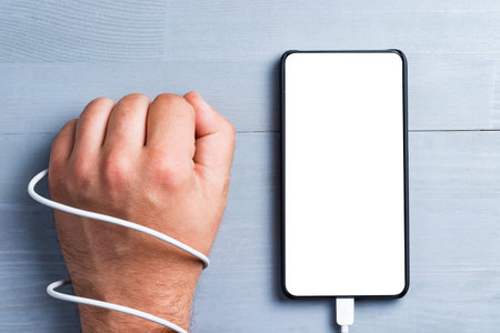 Hand tied with cable and bezel less smart phone with blank screen on a wooden background. Addiction...