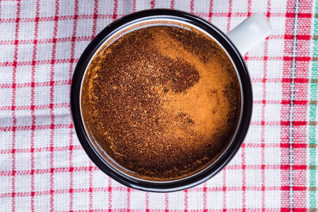 Coffee in a vintage metal mug on  red and white kitchen towel.