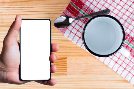 Bezel less smart phone with blank screen in a hand. Empty cup, lavender, spoon and vintage kitchen towel.の写真素材