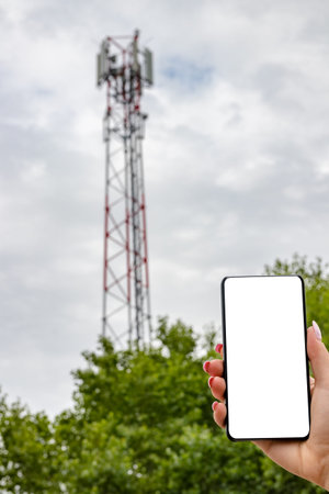 Hand holding bezel less smart phone with blank screen against cell tower background.の写真素材