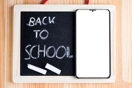 Back to school written on a blackboard with bezel less smart phone and chalk. Traditional vs modern learning abstract concept.の写真素材