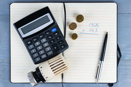 Home heat savings or expenses concept. Radiator regulator with coins and calculator on a notepad.の写真素材