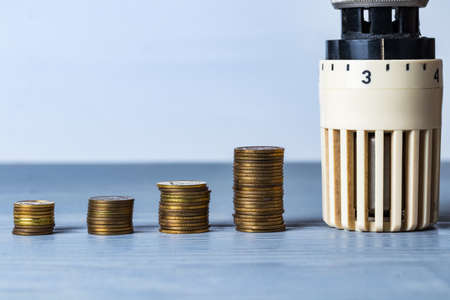 Home heat savings or expenses concept. Radiator regulator with coin stacks.の写真素材