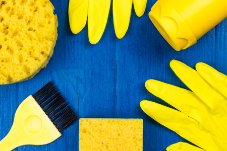 Yellow cleaning supplies on a blue background. Copy space in the center with frame. Flat lay top...