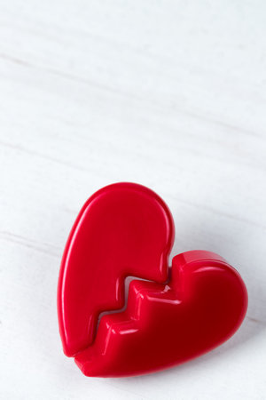 Broken red Valentines Day heart on white wooden background. Vertical orientation. Copy space on top.の写真素材