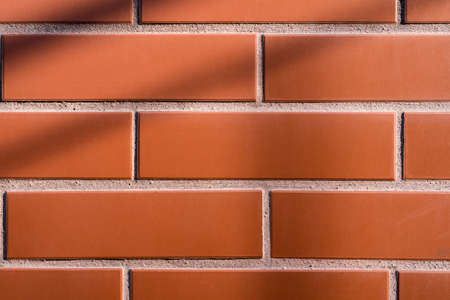 Red brick wall with shadows as a background. New, elegant home construction.の写真素材