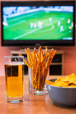 Watching football or soccer on television with beer, chips and breadsticks.の写真素材