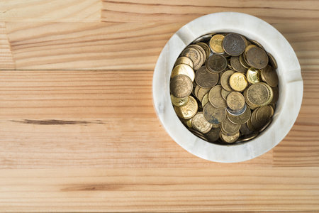 Coins in marble ashtray on natural wooden background. Burning money smoking cigarettes abstract...