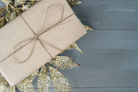 Present for Christmas wrapped in natural organic recycled paper on golden ornament on wooden background. Copy space on the right.の写真素材