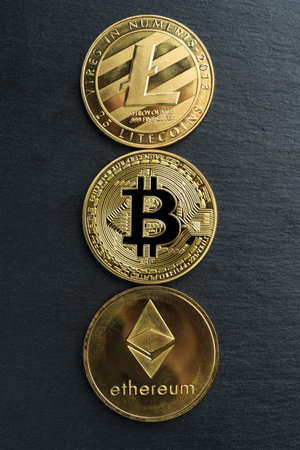 Physical Bitcoin, Litecoin and Ethereum gold coins on a black stone slate plate background....