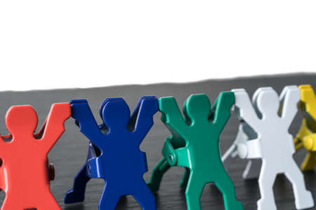 Colorful diverse miniature people figurines standing in a row on a dark stone slate plate. Isolated on white background. Diversity abstract concept.の写真素材