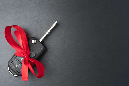 Car key with red bow on dark black slate plate background. Christmas or Valentine's Day gift or present abstract concept. Copy space on the right. Flat lay top view.の写真素材