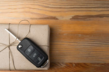 Car key on a box wrapped in paper with twine bow on natural wooden table background. Christmas or Valentine's Day gift or present abstract concept. Copy space on the right. Flat lay top view.の写真素材