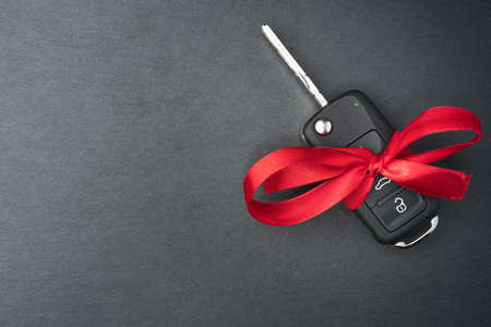 Car key with red bow on dark black slate plate background. Christmas or Valentine's Day gift or present abstract concept. Copy space on the left. Flat lay top view.の写真素材