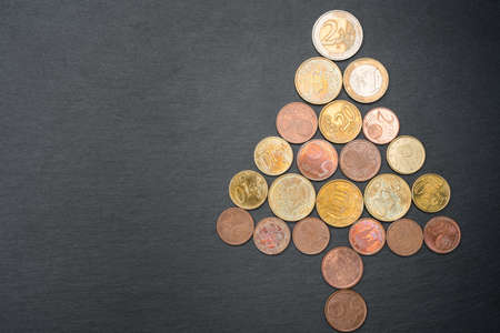 Christmas tree made out of Euro coins on dark black slate plate background. Copy space on the left. Flat lay top view.の写真素材