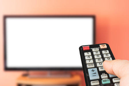 Caucasian man watching TV at home with white screen. Changing channels and adjusting volume with...