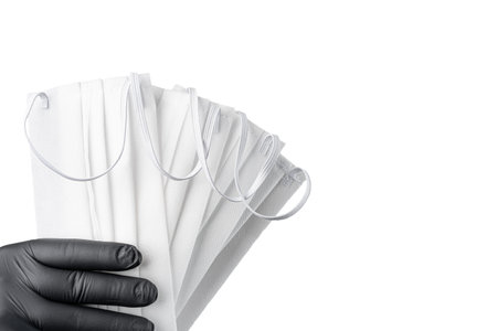 Hand in black protective glove holding bunch of face masks. Isolated on white background. Copy space...