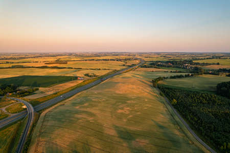 Aerial view of highway or motorway beetween fields in a countryside during sunsetの写真素材