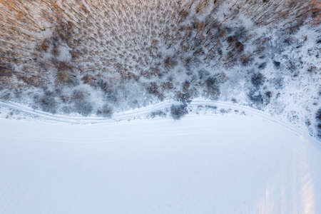 Aerial top down drone view of a road on winter snow covered fields and forest at sunsetの写真素材