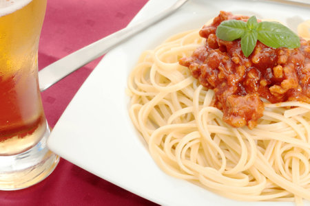 dish of noodles with tomato sauce and minced meat and beer glass in the foreground on a red backgroundの写真素材