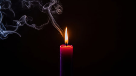 Lit candle with smoke rising in the darkの素材