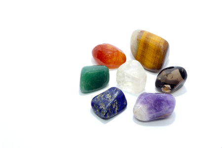 Chakra stones on white background - multi colored tumbled crystal gem stones shaped to form an...
