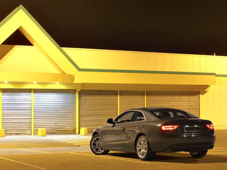 Grey Audi A5 Sport Coupe in front of a yellow factory building at night.の写真素材