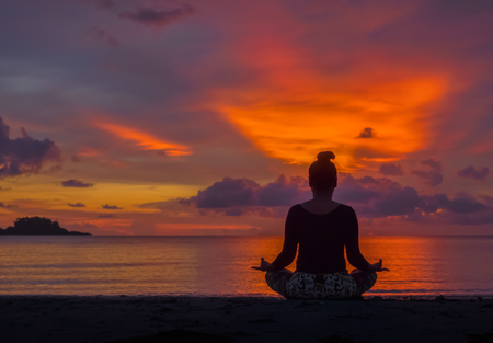 Silhouette of woman sit on the beach practice yoga at sunsetの写真素材