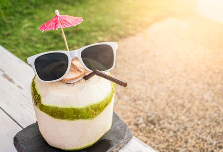 Fresh coconut juice wearing sunglasses on wood white table in sunlightの写真素材