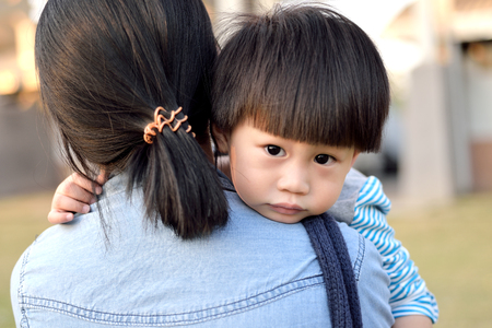 Young boy looking over mother's shoulderの写真素材
