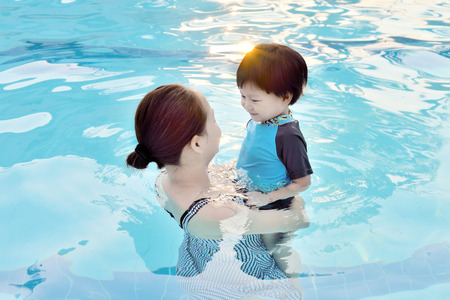 Young mother and her son having fun in a swimming poolの写真素材