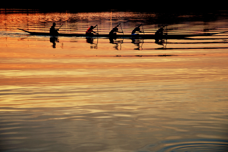 Team work of young men in a row boat silhouetted at sunsetの写真素材