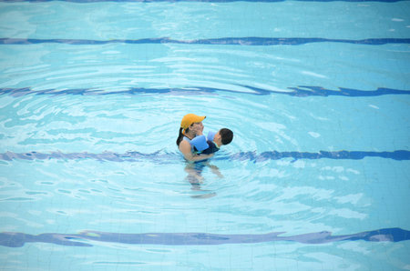 Happy young mother and her little son having fun together in an outdoor swimming pool