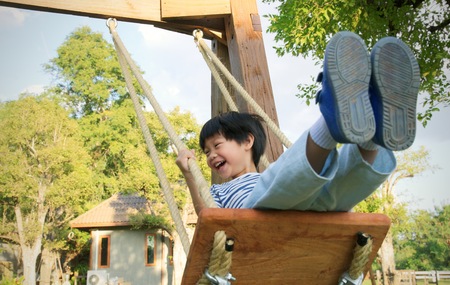 Happy little asian boy laughing and swinging on a swingの写真素材