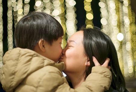 Young asian mother kissing her son on yellow round bokeh backgroundの写真素材